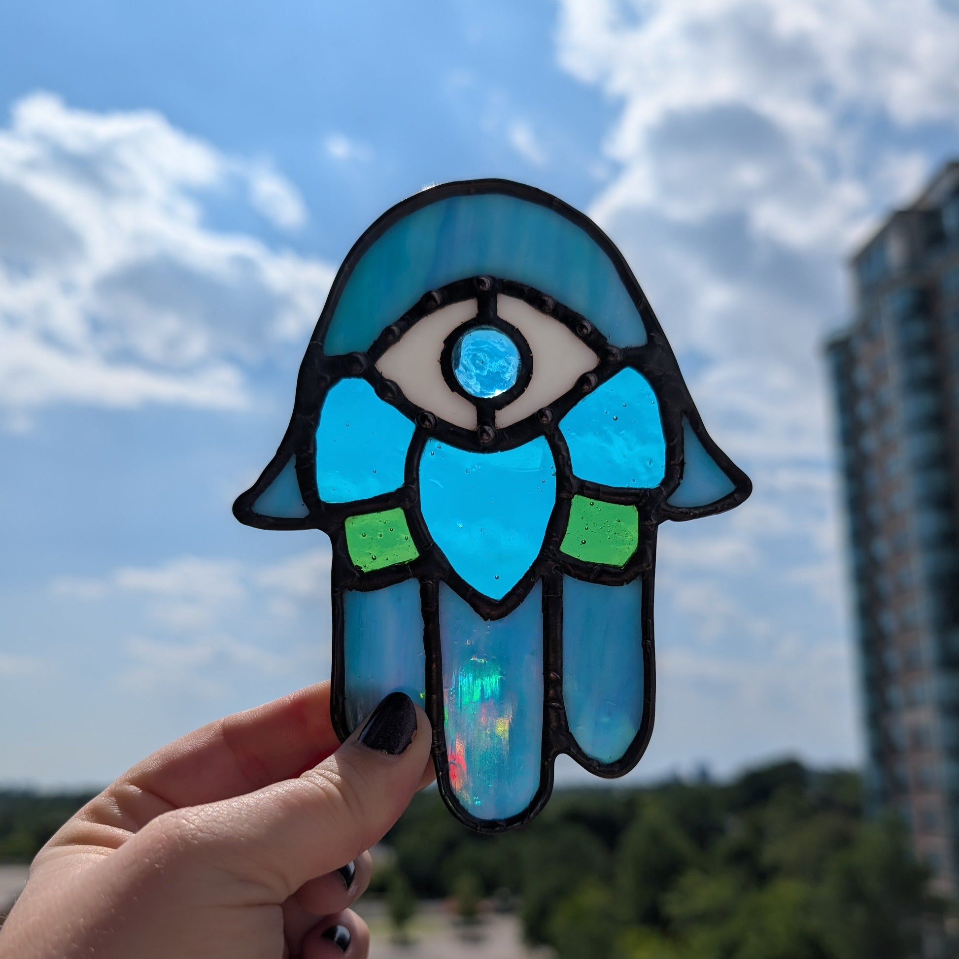 Handheld blue stained glass Hamsa with an eye design against a cityscape background